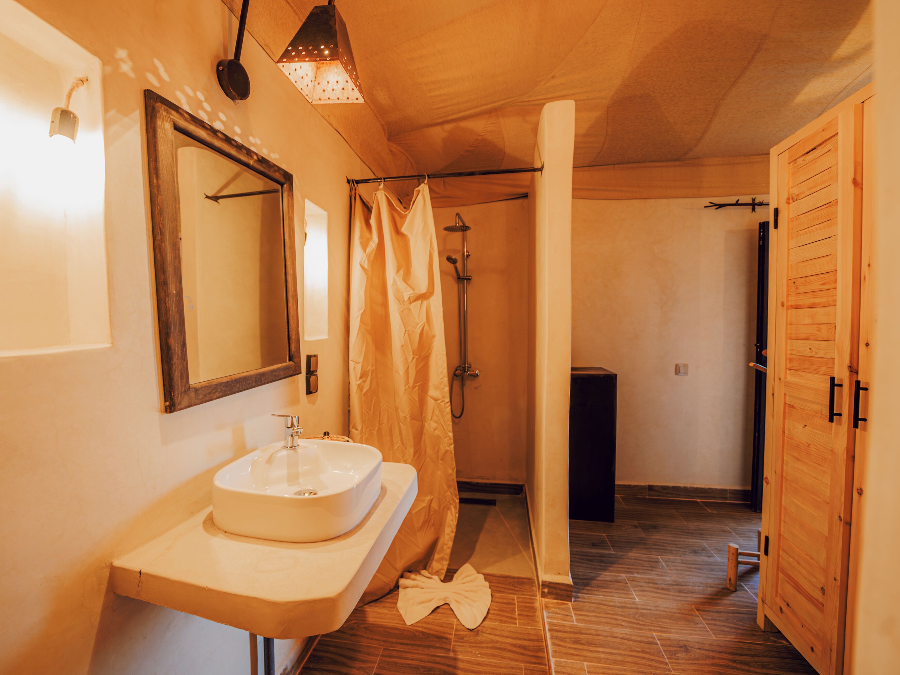 A bathroom with a wooden vanity, a mirror, a shower area, and a wooden door.