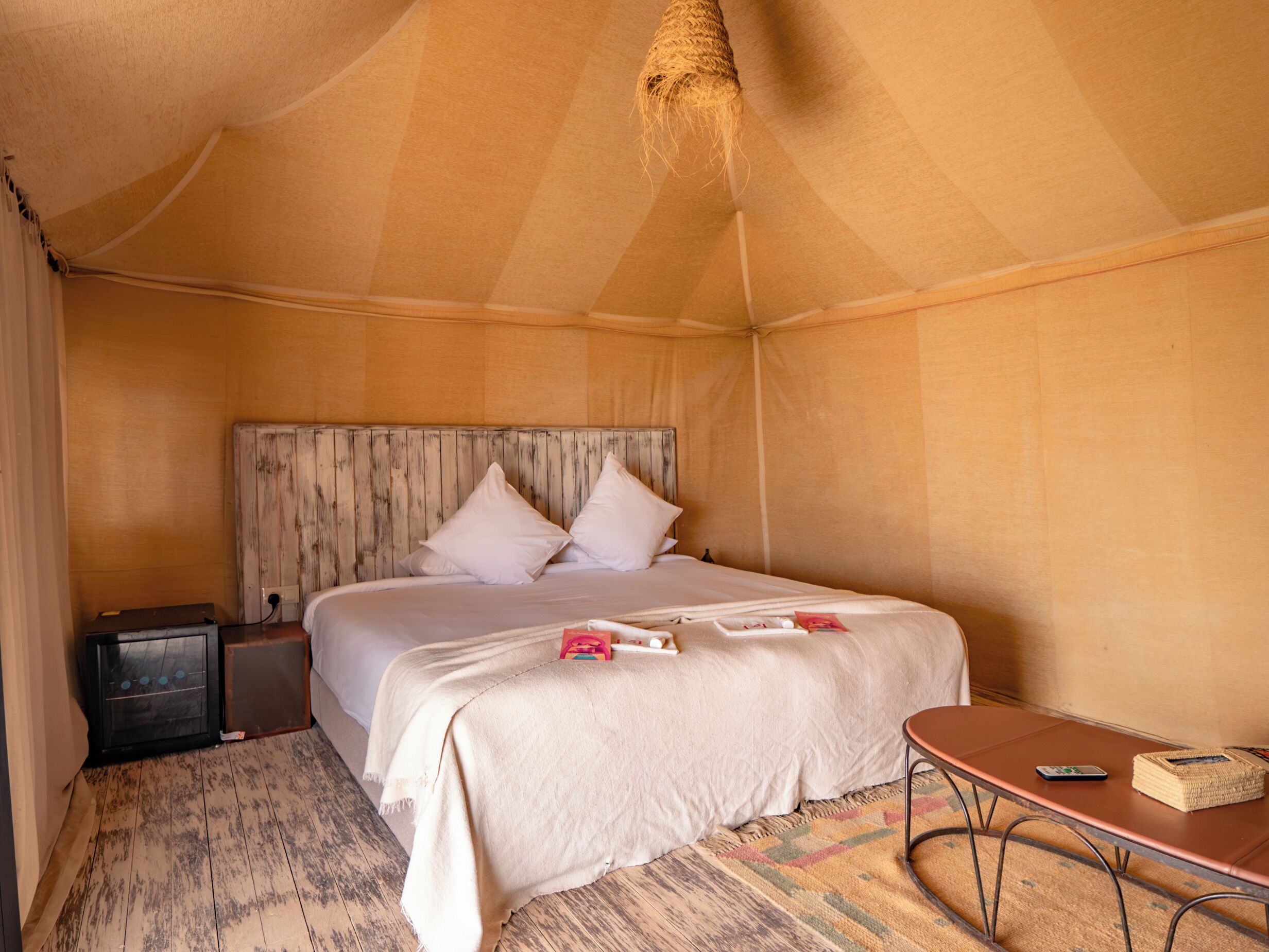 A tent-style room with a bed, bedside table, and a small table with a basket.
