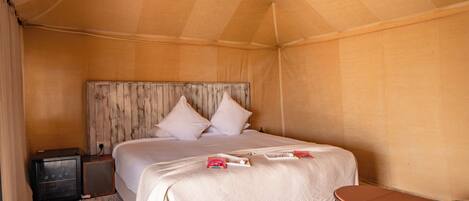 A tent-style room with a bed, bedside table, and a small table with a basket.