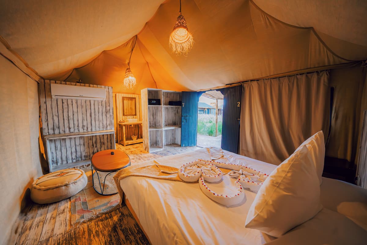 A tented room with a bed, a wooden wardrobe, a small table, and a hanging light fixture.