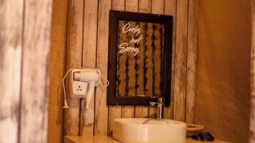 Um banheiro com parede de madeira, uma placa emoldurada com a frase "Only hot water", uma pia branca e um secador de cabelo conectado.