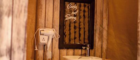 A bathroom with a wooden wall, a framed sign saying "Only hot water", a white sink, and a hairdryer plugged in.