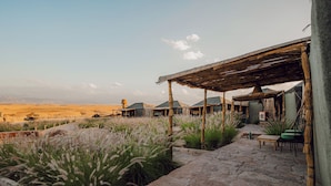 A rustic outdoor seating area with stone flooring, surrounded by tall grasses and a view of a desert landscape. - Le Bedouin Agafay (Agafay)