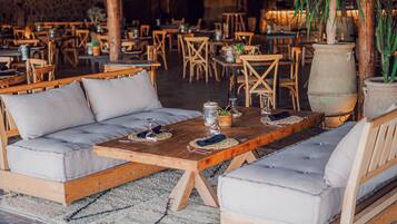 A cozy seating area with cushioned sofas and a wooden table, surrounded by rustic decor and plants.