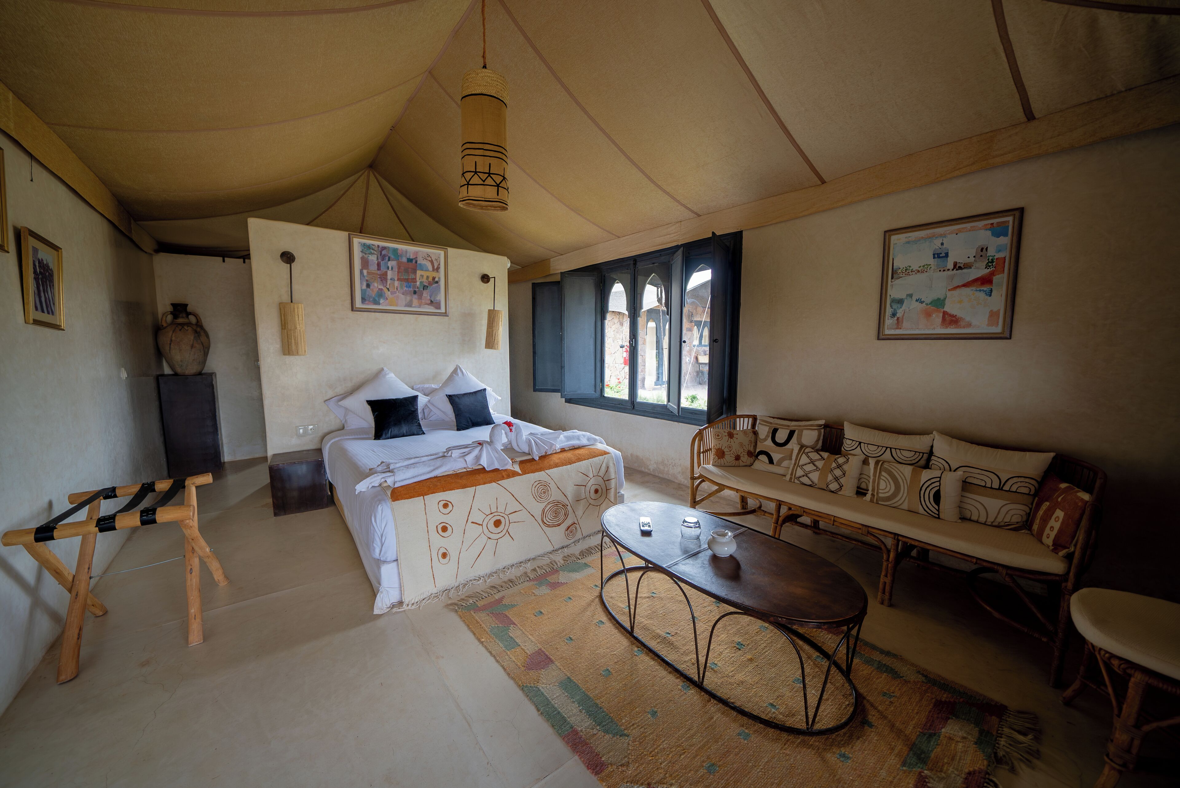 A cozy room with a bed, a sofa, a small table, and a hanging light fixture.