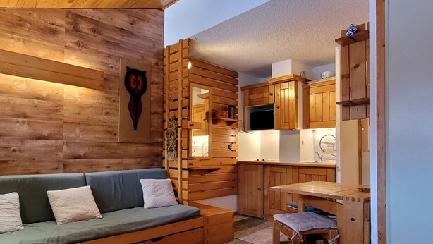 Um quarto acolhedor estilo cabana, com parede de madeira, um sofá, uma pequena mesa de jantar e armários de madeira.