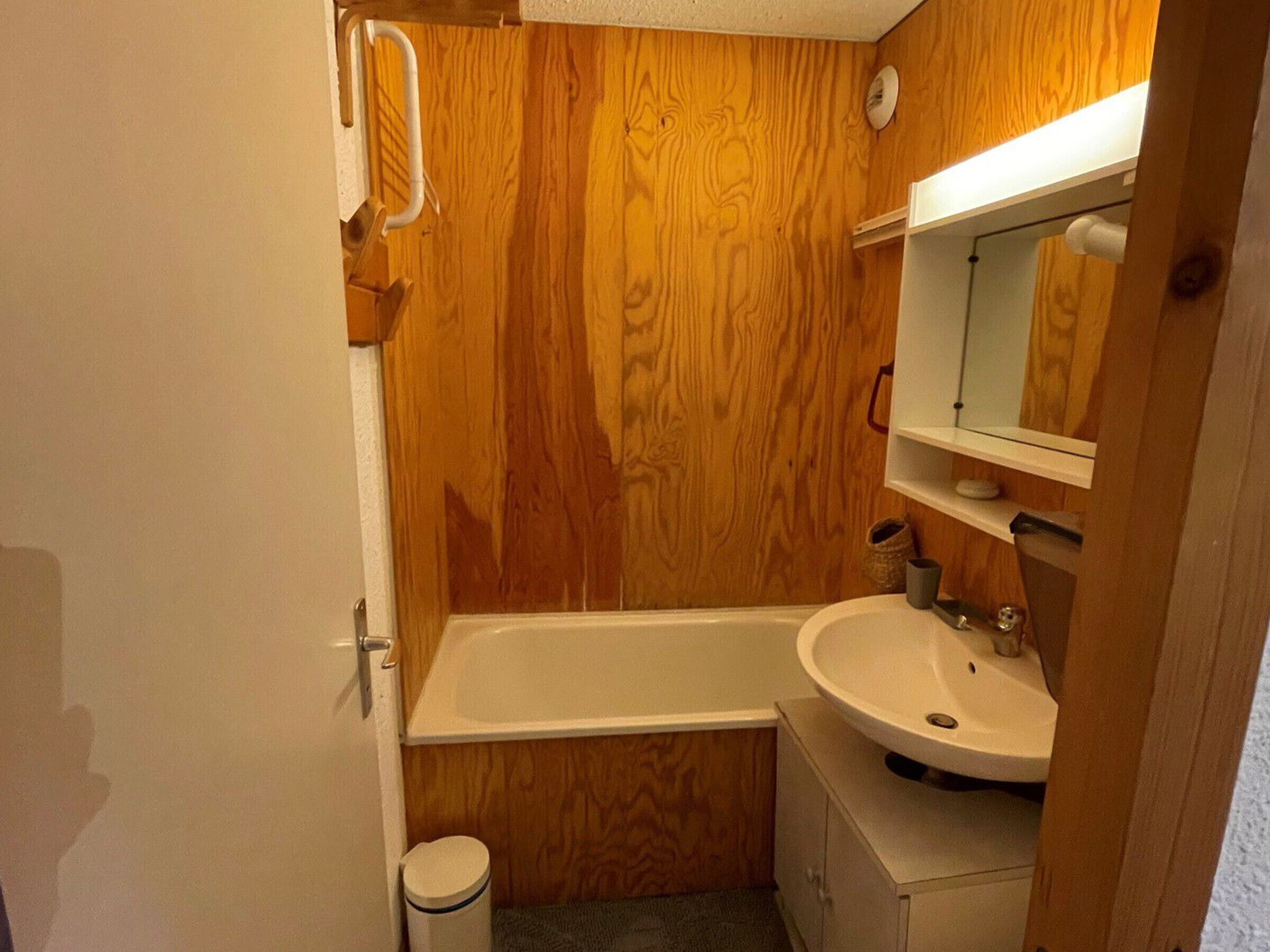 A small bathroom with wooden walls, a white sink, and a bathtub.