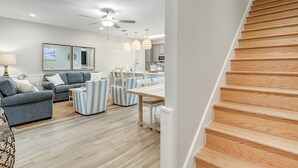 Una sala de estar moderna con un sofá, sillones y una mesa de comedor. Una escalera conduce a un nivel superior.