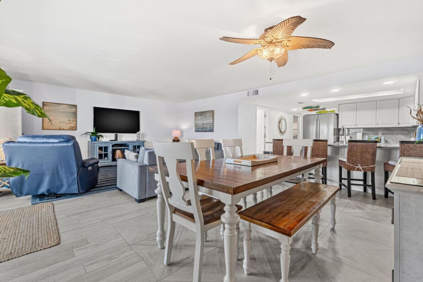 Un salon moderne avec une table à manger en bois, des chaises blanches, un canapé bleu et un ventilateur de plafond.