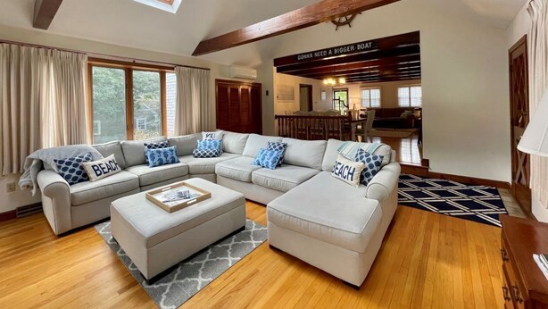 A spacious living room with a large L-shaped sectional sofa, a small ottoman, and a ceiling fan. A sign on the wall reads "GONNA NEED A BIGGER BOAT." - Dog friendly home with large backyard! (North Chatham)
