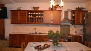 A kitchen with wooden cabinets, a marble countertop, a stove, and a dining table with chairs. - Platanus Gardenhouse (Saronikos)