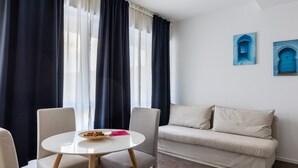 Ein Zimmer mit einem runden Tisch, zwei Stühlen, einem Sofa und einem Fenster mit Vorhängen.
