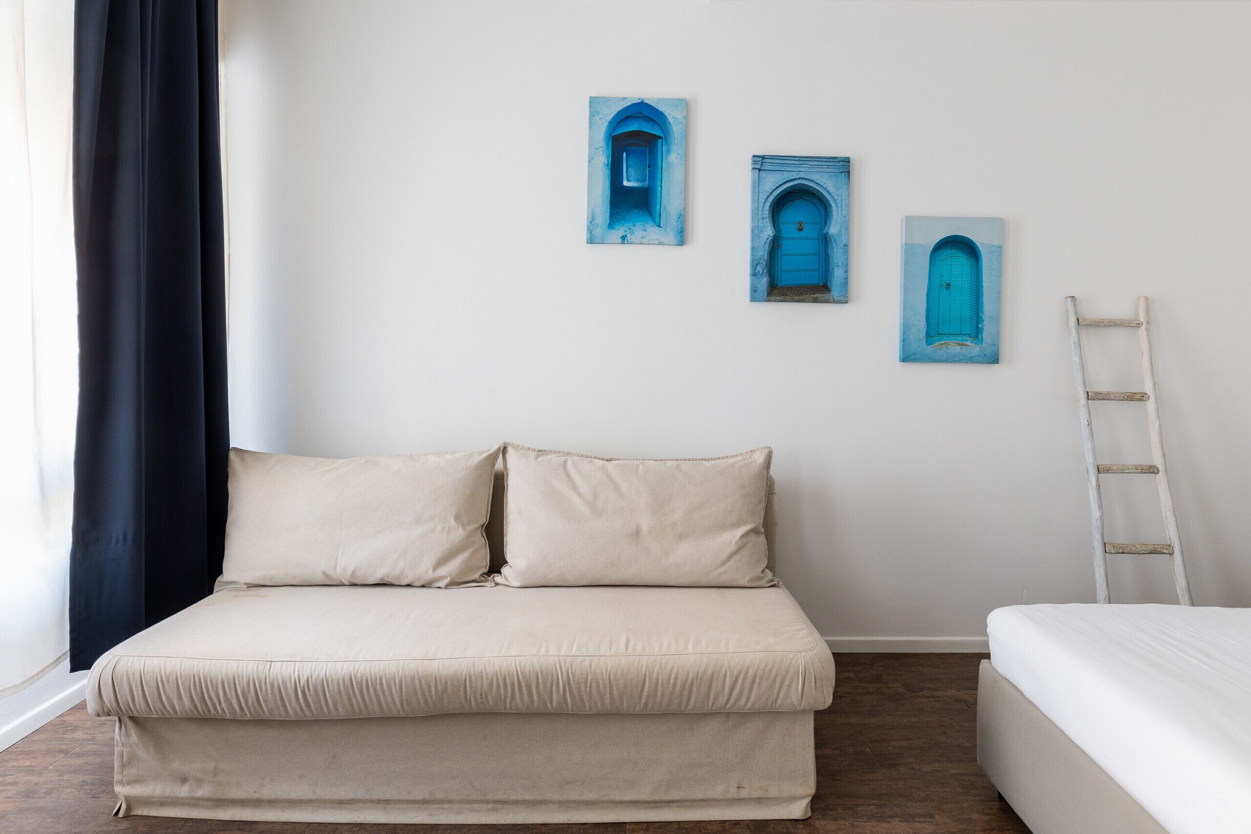 A room with a bed, a sofa, and three blue door paintings on the wall.