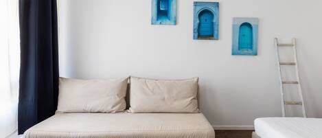 A room with a bed, a sofa, and three blue door paintings on the wall.