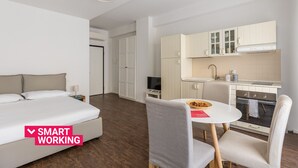 Ein modernes Hotelzimmer mit Bett, einem kleinen Esstisch und einer Küchenzeile.