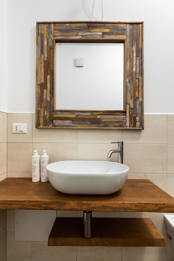 A bathroom with a wooden vanity, a white sink, and a mirror with a wooden frame.