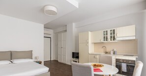 A modern hotel room with a bed, a small dining table, and a kitchenette.