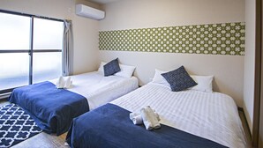 Hotellihuone, jossa on kaksi sänkyä, suuri ikkuna, kuvioitu seinä ja kattotuuletin.