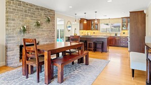 A spacious kitchen with a stone wall, wooden dining table, and bar stools. - Wine Country Retreat w/ Pool, Hot Tub, Backyard & Game Nights Near Wineries (Santa Rosa)