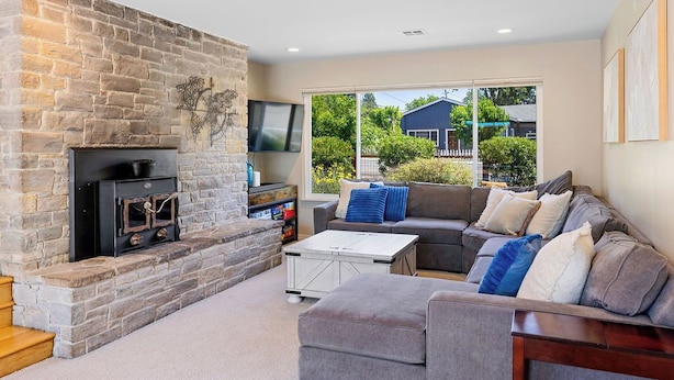 A living room with a stone fireplace, a sectional sofa, and a television. - Wine Country Retreat w/ Pool, Hot Tub, Backyard & Game Nights Near Wineries (Santa Rosa)