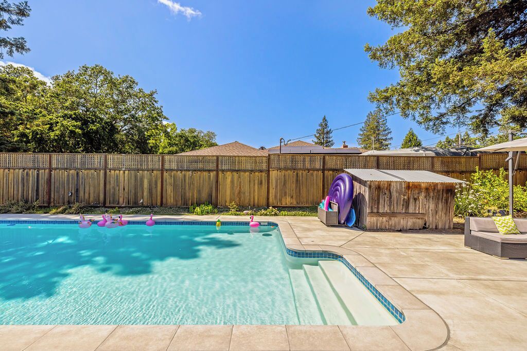 A backyard with a swimming pool, a wooden fence, and a small outdoor seating area.