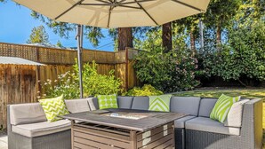 An outdoor patio with a wooden table, cushioned seating, and a large umbrella. - Wine Country Retreat w/ Pool, Hot Tub, Backyard & Game Nights Near Wineries (Santa Rosa)