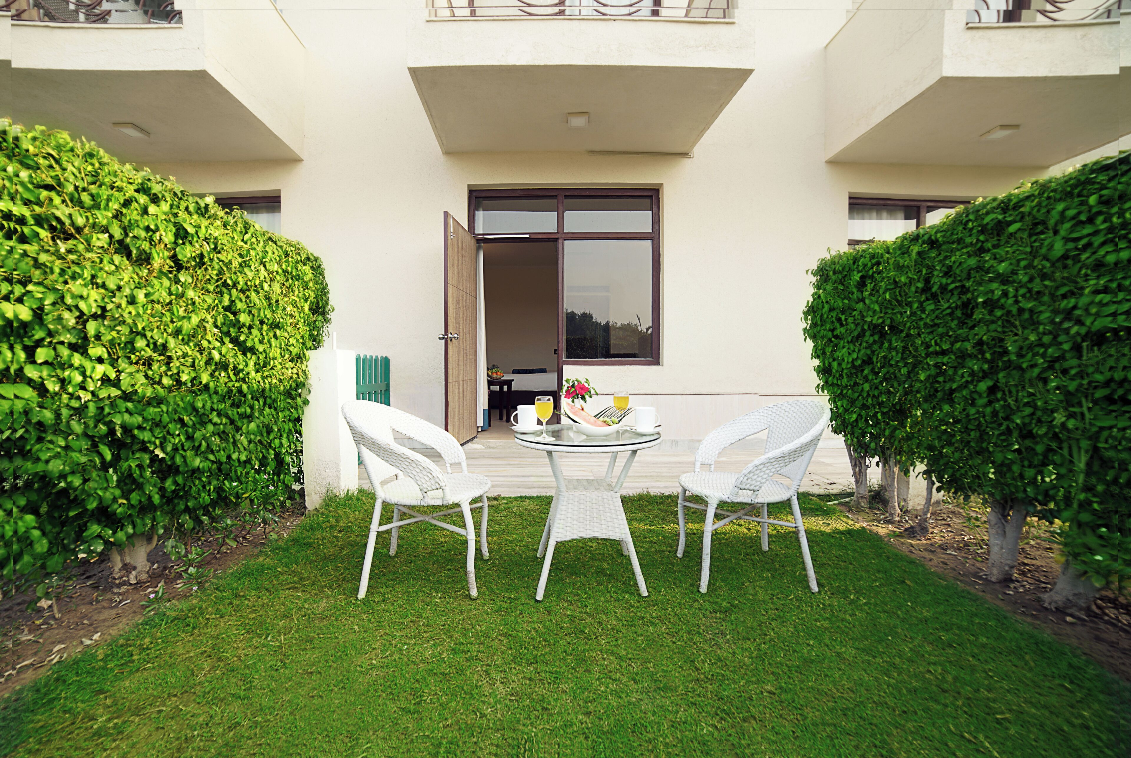 A courtyard with a table and chairs, surrounded by hedges and a building entrance.