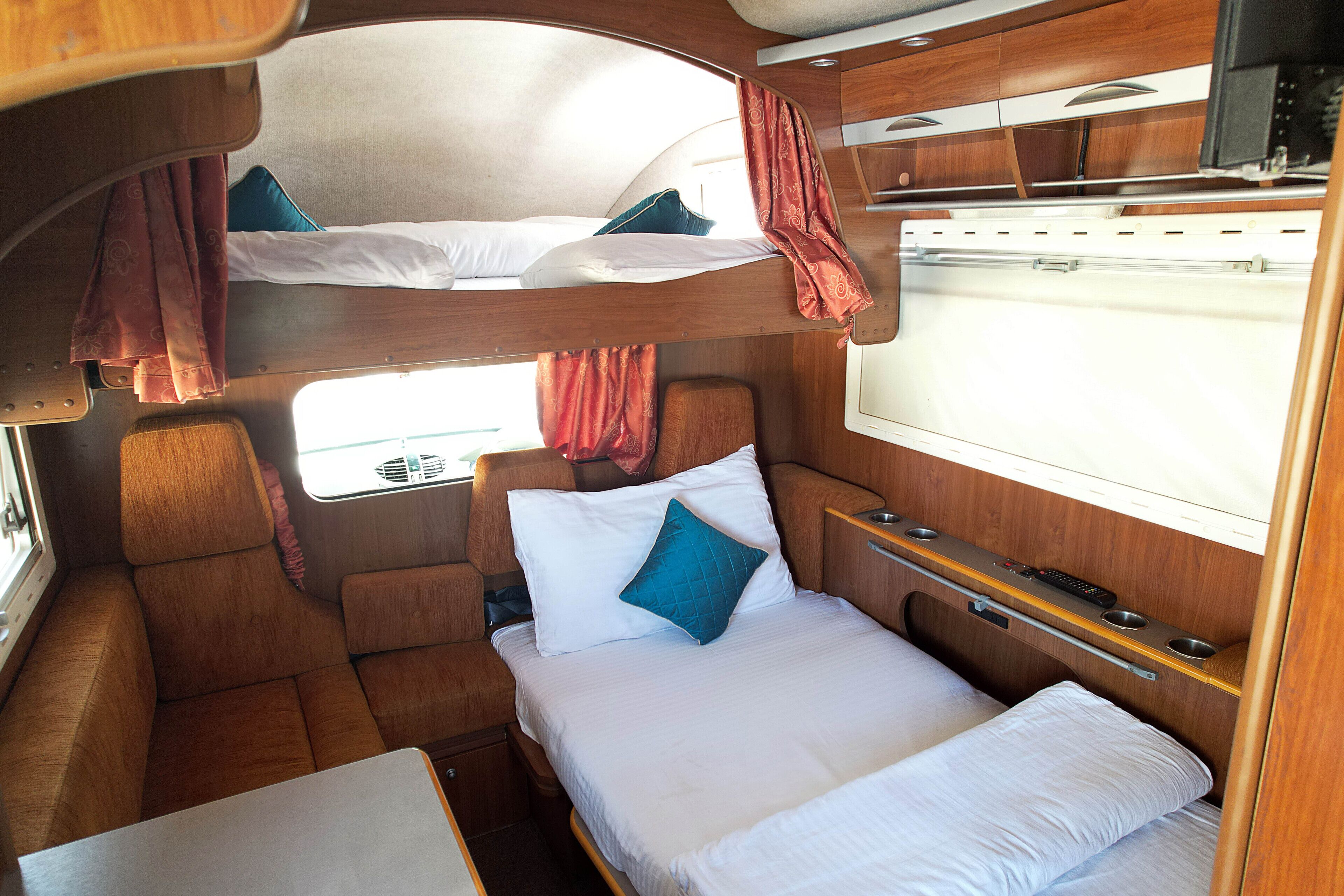 Un interior compacto y bien organizado con una litera, una cama individual y una pequeña mesa.