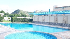 A swimming pool with a hot tub in the center, surrounded by a tiled deck. - TreeHouse Sunrise Resort & Caravan Park (Neemrana)