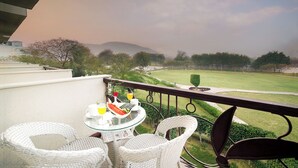 A balcony with wicker chairs and a glass table set with breakfast items, overlooking a well-manicured lawn and distant hills. - TreeHouse Sunrise Resort & Caravan Park (Neemrana)