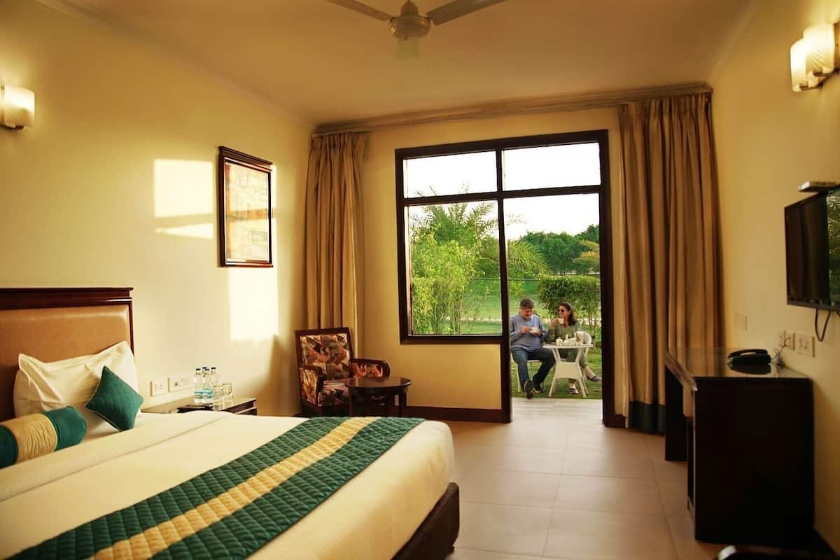 A hotel room with a bed, a chair, a table, a TV, and a view of the outdoors.