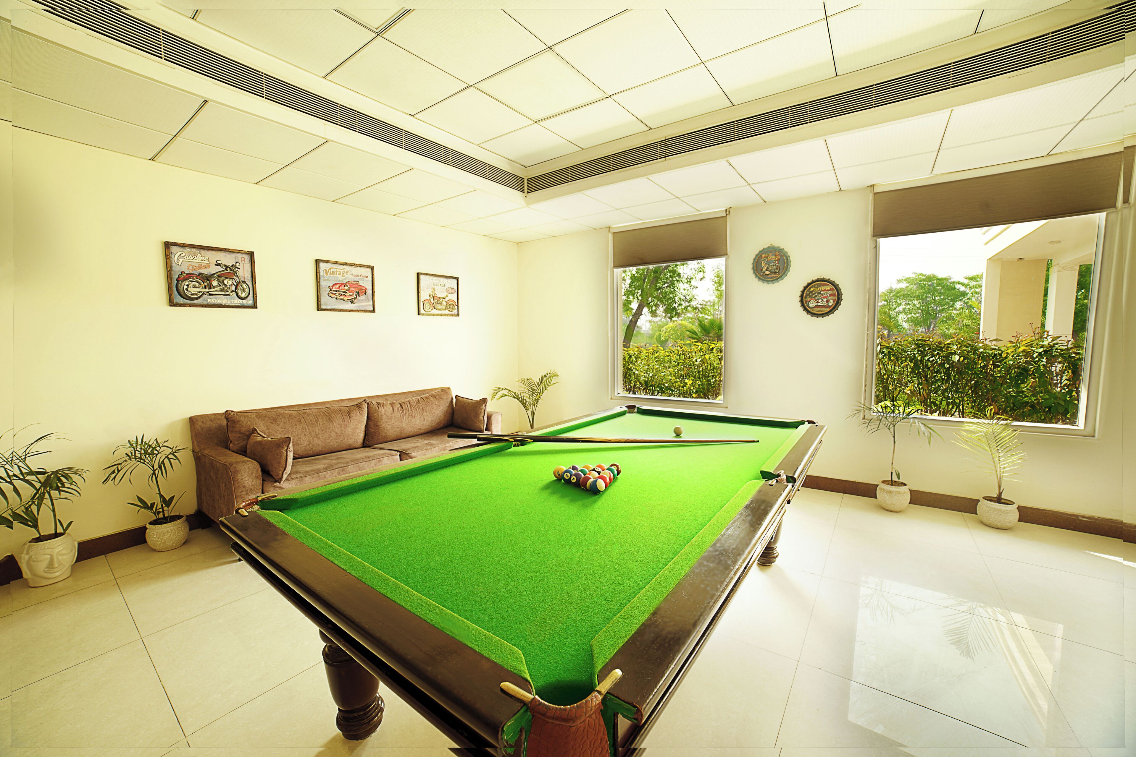 A pool table with a green felt surface, a brown sofa with cushions, and several potted plants.