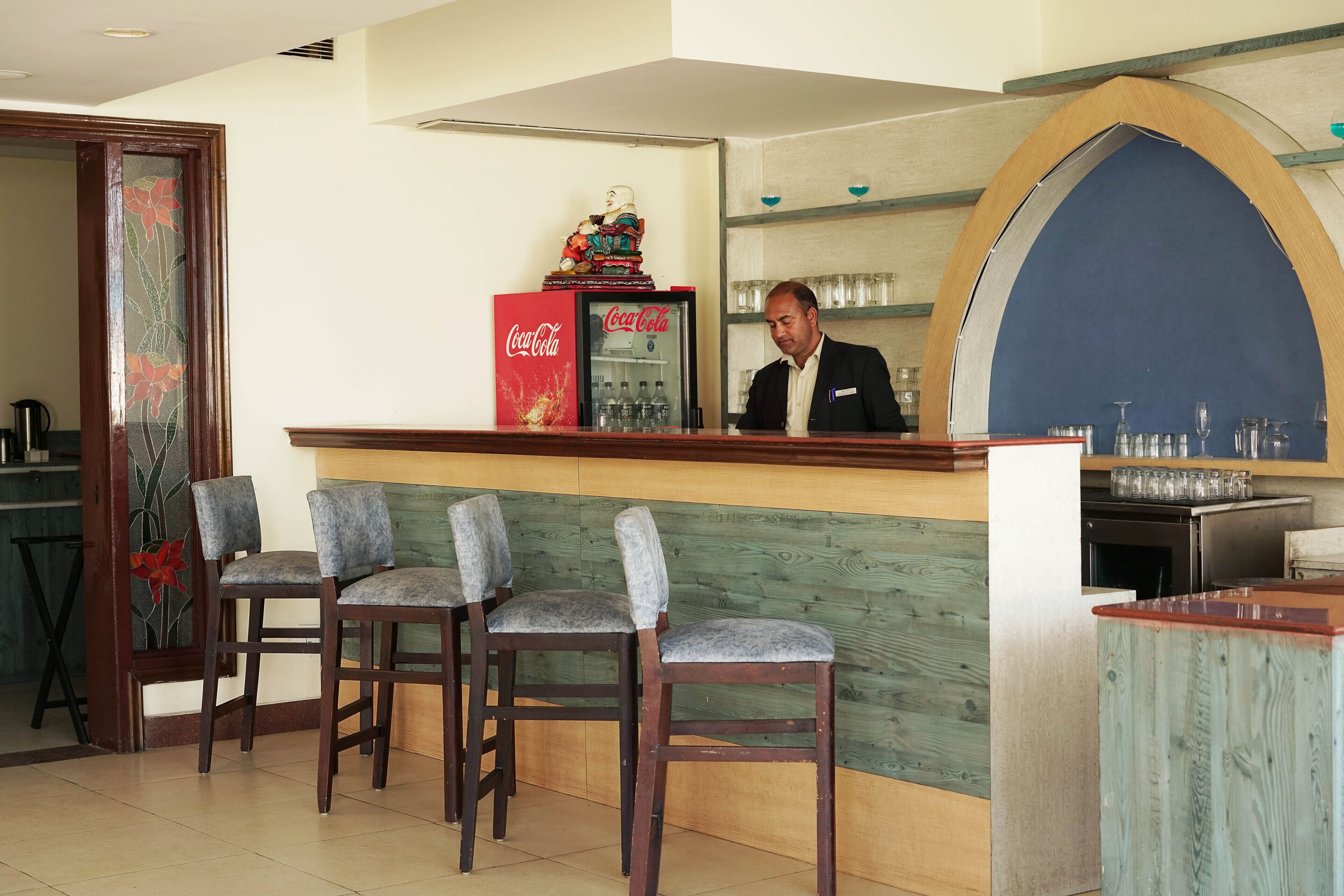 Eine Barbereich mit einem Coca-Cola-Kühlschrank, einer Holztheke und Barhocker.