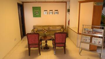 A lobby with a sofa, two chairs, a small table with a vase, and a CCTV sign.