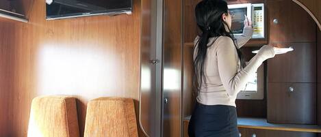 Una mujer parada en una cabaña con un microondas y un armario de madera.