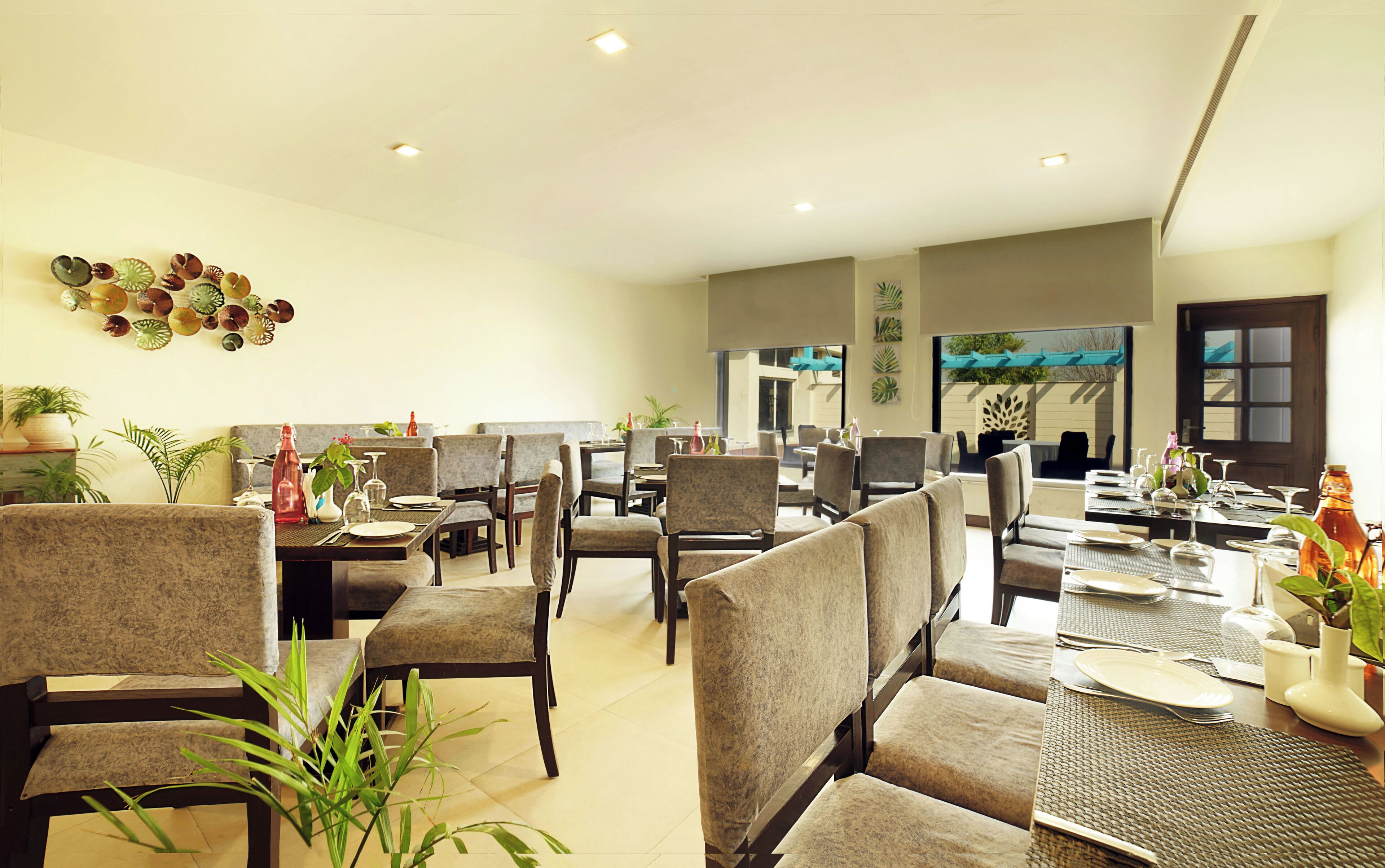 A spacious dining area with multiple tables and chairs, a decorative wall with plant arrangements, and a view of the outdoors through large windows.