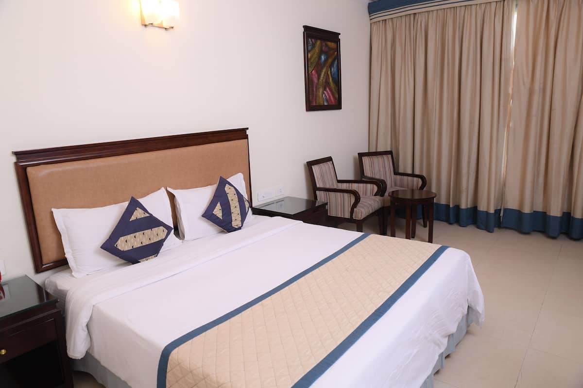 A hotel room with a bed, a chair, a desk, and a window with curtains.