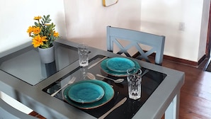 A dining area with a glass table, teal plates, and a potted plant. - Catherine Suites (Willemstad)