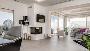 A spacious living area with a modern design, featuring a fireplace, seating arrangements, and large windows offering a view of the outdoors. - Balia Suites (Corfu)