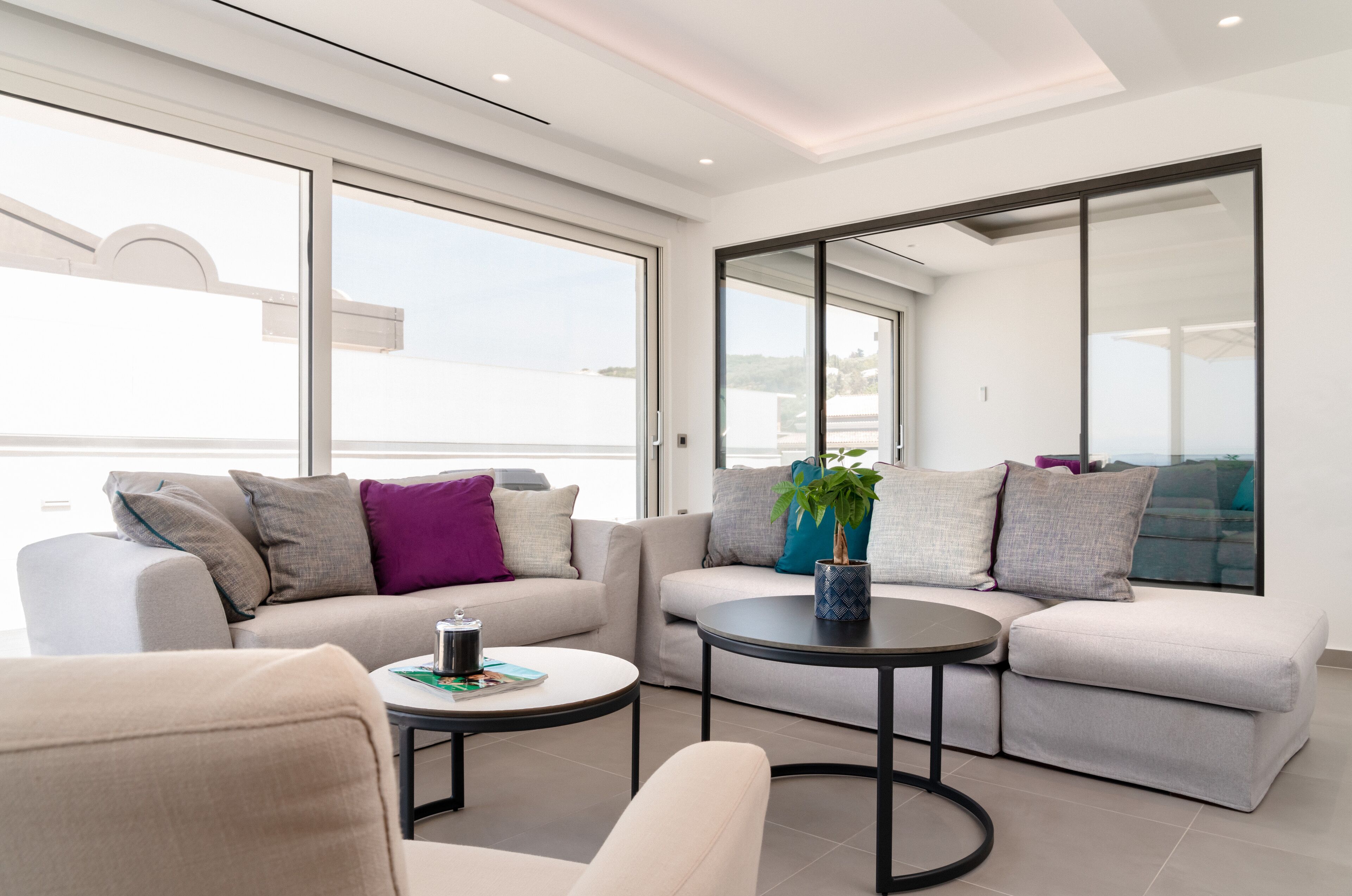 A modern living room with a sofa, a coffee table, and a large window offering a view of the sea.