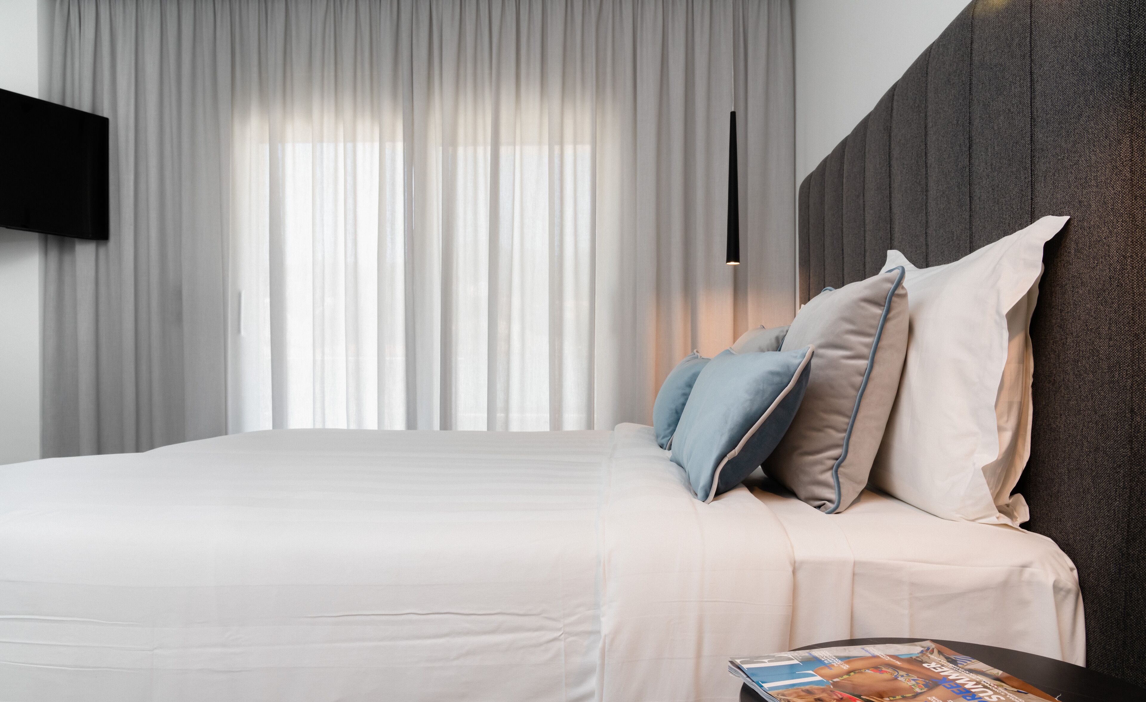 Een moderne slaapkamer met een groot bed, een flatscreen televisie aan de muur en een tijdschrift op het nachtkastje.