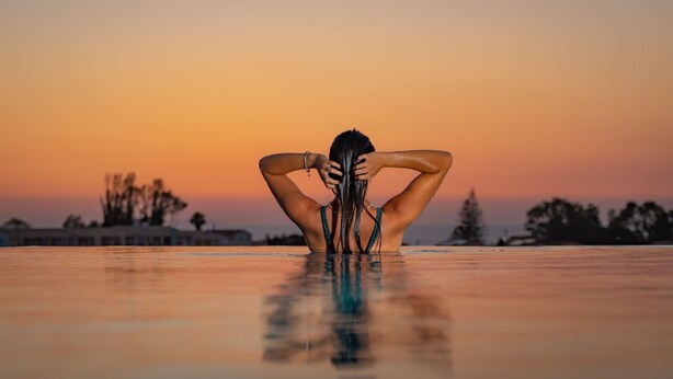 A person standing in a pool with a sunset in the background. - Balia Suites (Corfu)