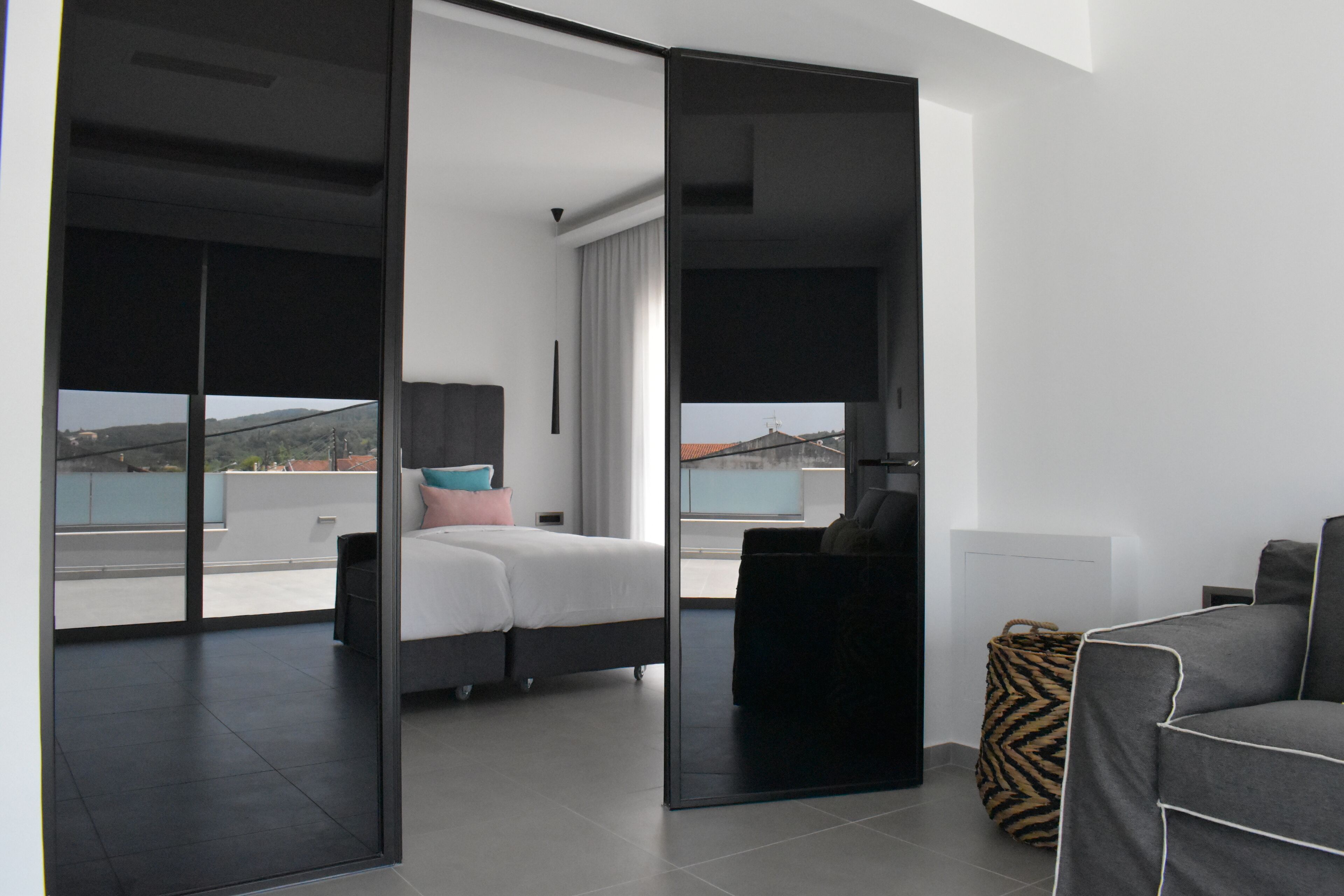 A modern hotel room with a balcony, a bed with multiple pillows, a sofa, and a large mirror.