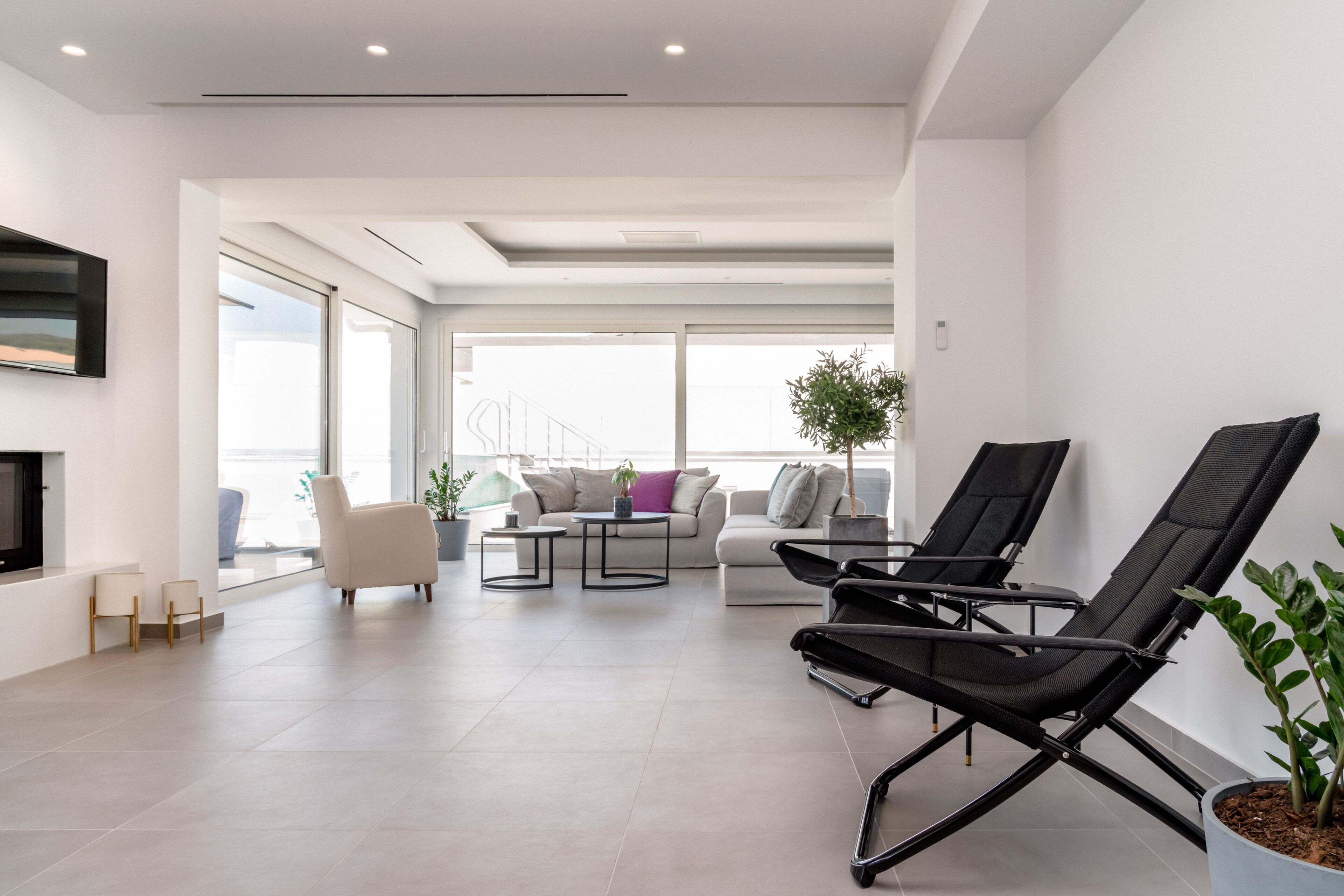 Un vaste espace de vie comprenant un canapé, deux fauteuils noirs, une table basse et un téléviseur fixé au mur.