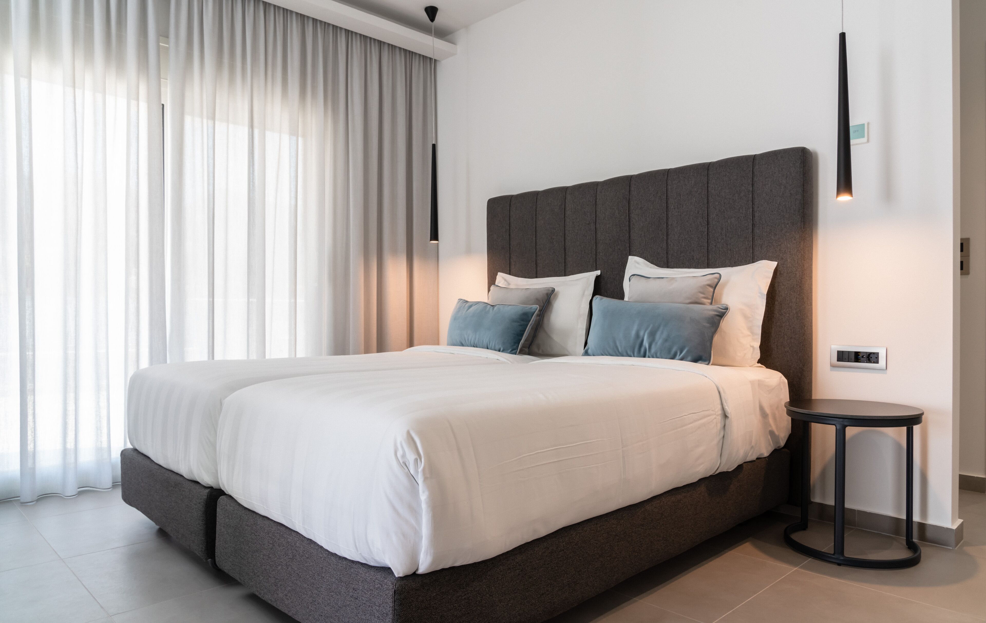 Un dormitorio moderno con una cama grande, cabecera gris y una mesita de noche.