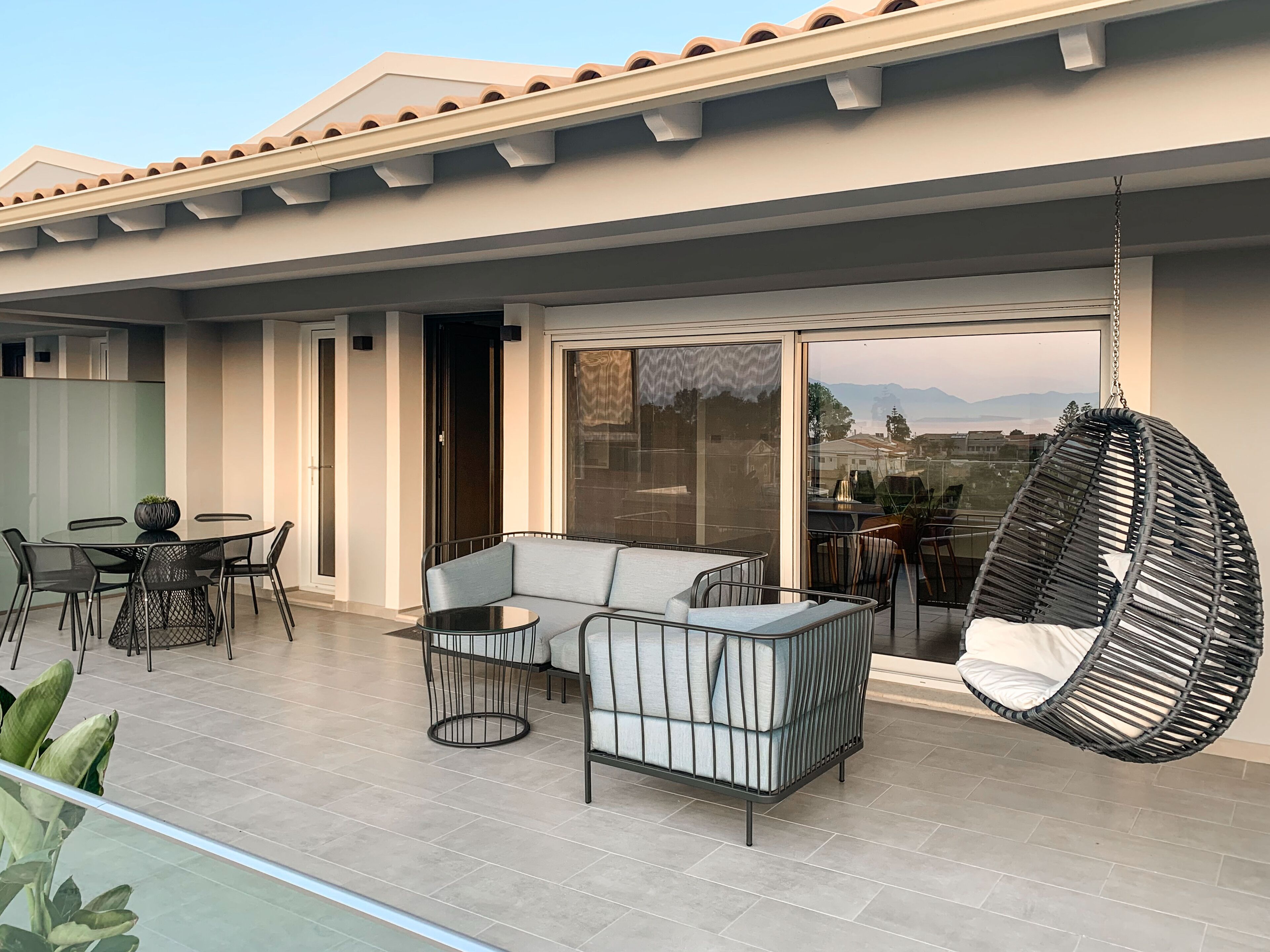 A modern outdoor patio with a round table, a sofa, and a hanging chair.