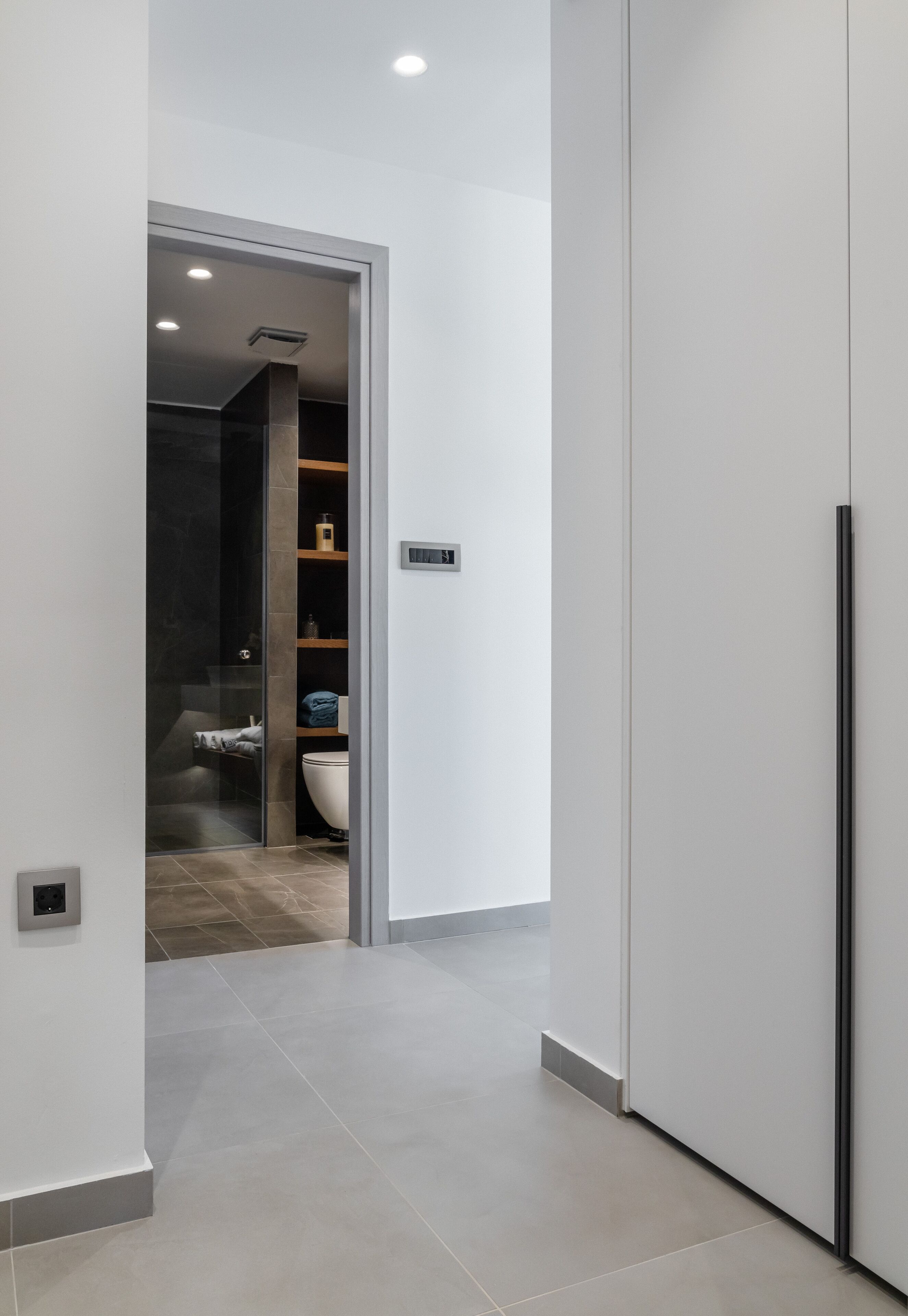 A modern bathroom with a glass shower enclosure, a white sink, and a dark tiled floor.