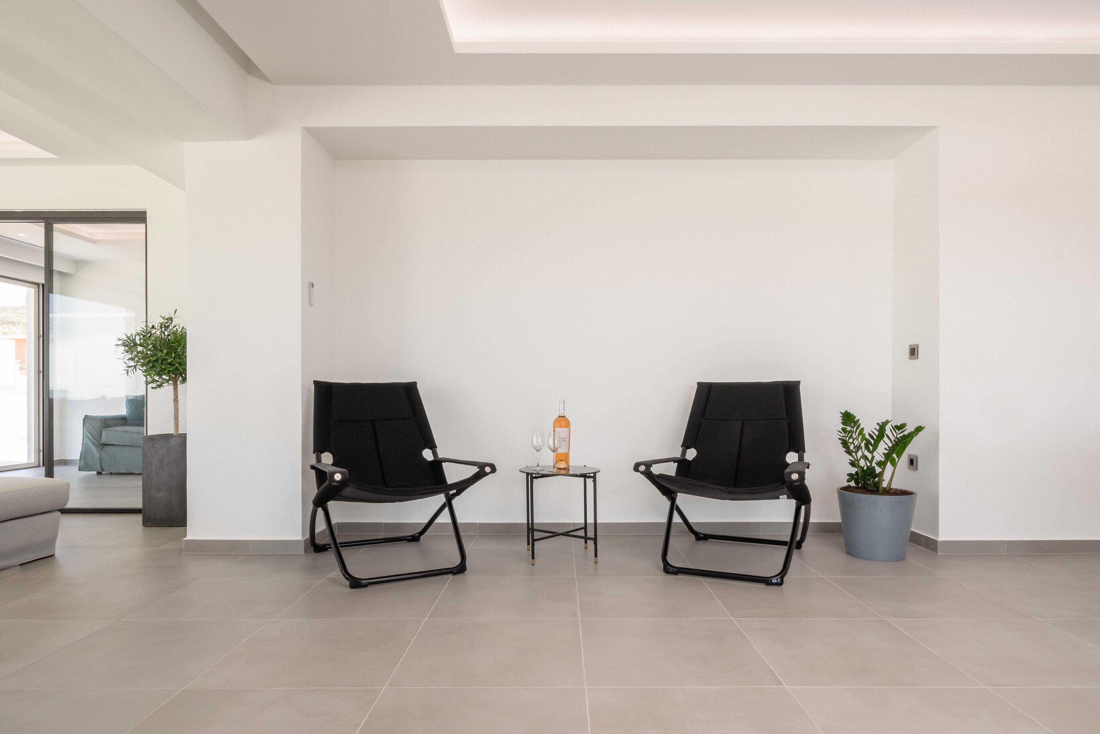 A modern room with two black chairs, a small table with a bottle and glass, and a potted plant.