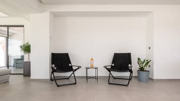 A modern room with two black chairs, a small table with a bottle and glass, and a potted plant.