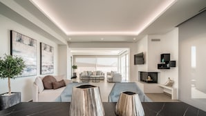 A modern living room with a dark marble table, two decorative vases, a sofa, and a television mounted on the wall. - Balia Suites (Corfu)